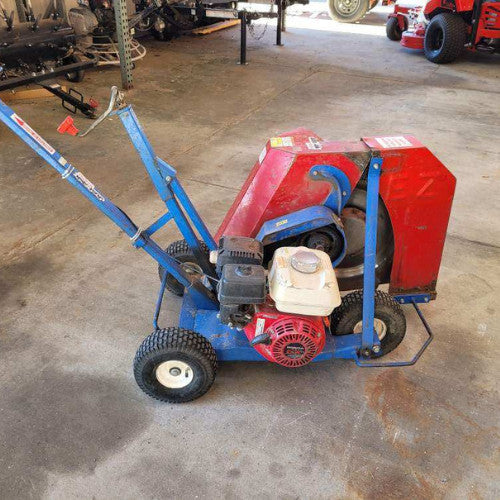 A blue and red lawn aerator with sturdy wheels is parked on a concrete garage floor. It has a weathered look, suggesting frequent use.