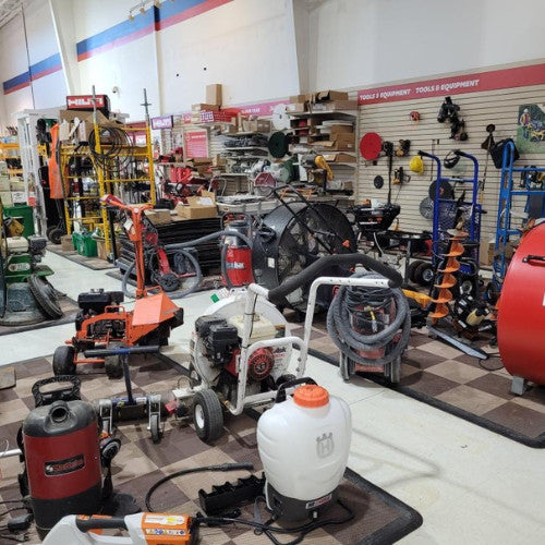 A cluttered tool rental store filled with various equipment including lawn mowers, fans, vacuums, and sprayers. Shelves are lined with tools and accessories.