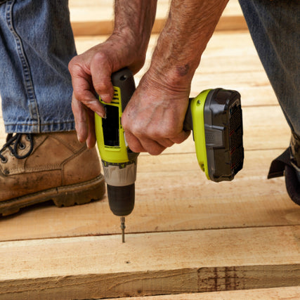 Contractor RentalsA person in jeans and work boots uses a green cordless drill to drive a screw into wooden planks, conveying a sense of focus and craftsmanship.